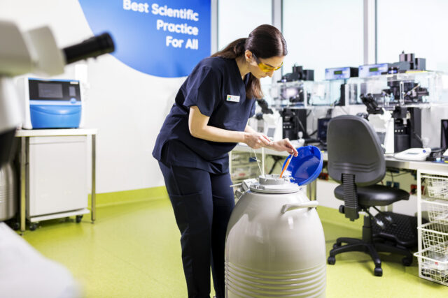 An embryologist pouring liquid nitrogen into a liquid nitrogen container storing frozen eggs and embryos.